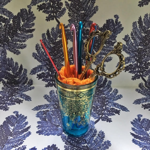 A Turkish tea glass filled with crochet hooks and a pair of vintage scissors.